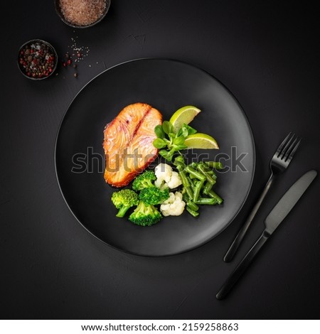 Baked salmon with vegetables (broccoli, cauliflower and green beans) on black background. Mediterranean diet concept. Flat lay, top view, copy space