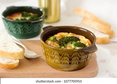 Baked scrambled eggs with broccoli, sausages and cheese served with slices of bread. Rustic style.
