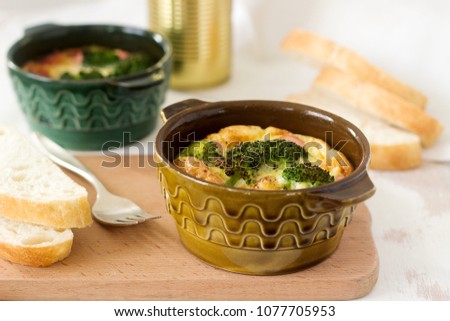 Baked scrambled eggs with broccoli, sausages and cheese served with slices of bread. Rustic style.