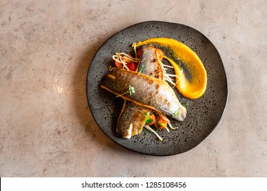 Baked sea bass on a black plate, grey background