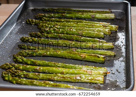 Baked seasoned asparagus on baking sheet with seasoning and olive oil
