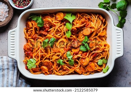 Baked spaghetti pasta with sausages in tomato sauce in the oven dish, top view.