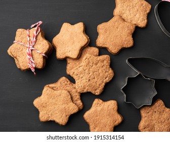 baked star shaped gingerbread cookies, wooden rolling pin and metal cutters on a black table, top view