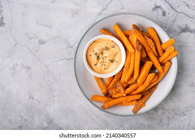 Baked sweet potato fries on a plate with savory sauce over concrete background, top view - Powered by Shutterstock