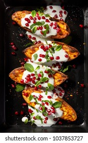 Baked sweet potatoes with garlic mint yogurt sauce sprinkled with pomegranate seeds and fresh mint leaves on a black background, top view. Delicious and healthy vegetarian meal