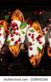 Baked sweet potatoes with garlic mint yogurt sauce sprinkled with pomegranate seeds and fresh mint leaves on a black background, top view, close-up. Delicious and healthy vegetarian meal.