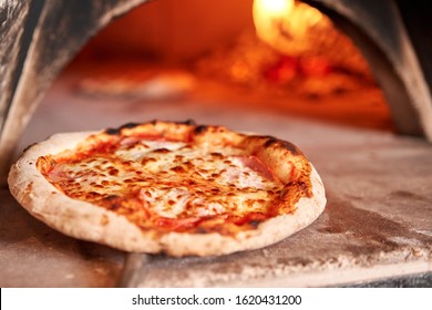 Baked tasty margherita pizza in Traditional wood oven in Naples restaurant, Italy. Original neapolitan pizza. Red hot coal.