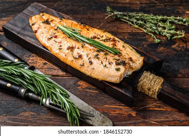 Baked trout fillet on a cutting board. Dark wooden background. Top view