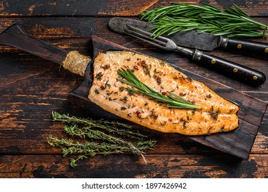 Baked trout fillet on a cutting board. Dark wooden background. Top view.
