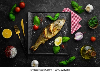 Baked trout with lemon and vegetables on a black stone plate. Seafood. River fish. Top view.