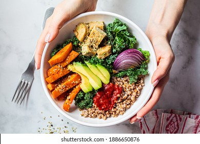 Baked vegetables, avocado, tofu and buckwheat buddha bowl. Vegan lunch salad with kale, baked sweet potato, tofu, buckwheat and avocado in a white bowl. Vegan concept.