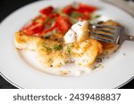 Baked whitefish fillet with creamy sauce served on plate with vegetables and greens.