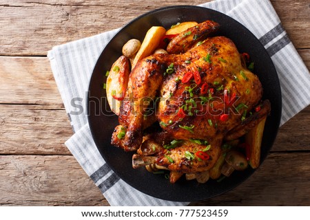 Baked whole chicken with mushrooms and potatoes close-up on a plate on a table. Horizontal top view from above