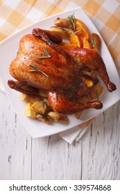baked whole chicken with oranges and potatoes close-up on a plate. vertical top view