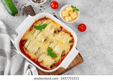 Baked zucchini rolls with ground meat, tomato sauce and cheese in a white baking dish on a gray concrete background. Selective focus, top view - Powered by Shutterstock