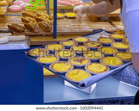 Baker arranging fresh-baked egg tarts into showcase at bakery