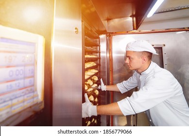 baker boy inserts a cart with raw dough baking trays into an industrial oven in a bakery. - Powered by Shutterstock