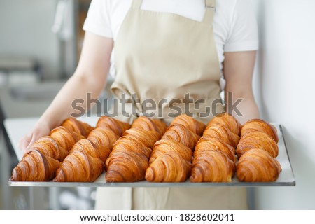 Baker carrying freshly baked crispy golden croissants on a metal tray to cool. Holding it by the sides.