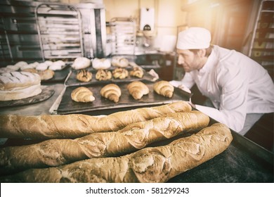 Baker checking freshly baked bread in kitchen of bakery - Powered by Shutterstock