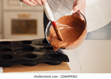 A baker or chocolatier prepares a chocolate cake by mixing melted chocolate with a spatula that drips onto the counter below. Pouring dough for a chocolate cake in a silicone mold for baking. - Powered by Shutterstock
