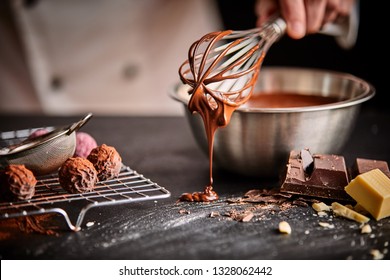 Baker or chocolatier preparing chocolate bonbons whisking the melted chocolate with a whisk dripping onto the counter below
