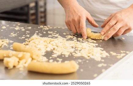 Baker coating cookie dough in almond slices on a work surface, preparing the dough for baking in a bakery, with hands arranging almond-covered dough in a professional setting - Powered by Shutterstock