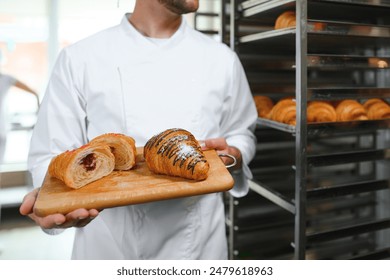 A baker cuts a croissant in a bakery and shows the jam filling. - Powered by Shutterstock