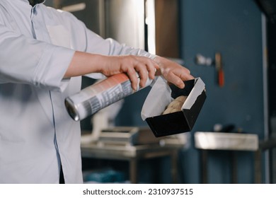 a baker greases a baking sheet with parchment paper and dough with oil from a professional spray bottle bakery production pastries - Powered by Shutterstock