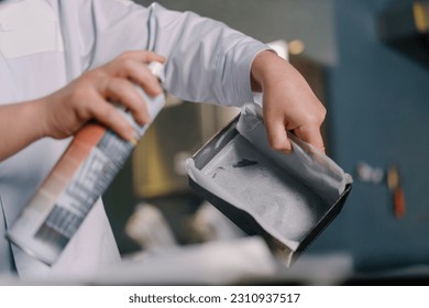 a baker greases a baking sheet with parchment paper and dough with oil from a professional spray bottle bakery production pastries - Powered by Shutterstock