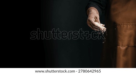 Baker hand dropping flour with dramatic light on dark background, artisan bread making concept with copy space for bakery banners and ads.