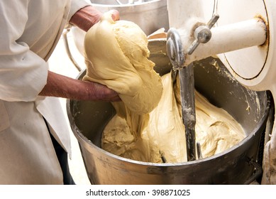 Baker holding a mound of raw dough in his hands above an industrial blending and mixing machine in his bakery in a close up view of his hands - Powered by Shutterstock