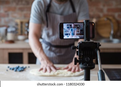baker online courses. food preparing and culinary training class concept. smiling bearded chef kneading dough in the kitchen and shooting video of himself using mobile phone on a tripod. - Powered by Shutterstock