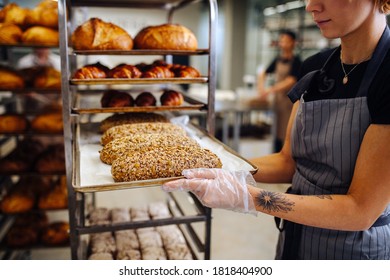 Baker placing metal tray with freshly baked crispy golden croissants on a shelf to cool. She's holding it by the sides in single use plastic gloves. - Powered by Shutterstock