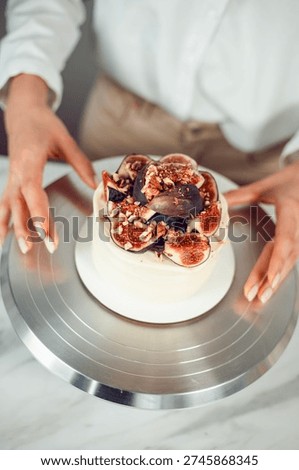 Baker prepares dessert with figs and nuts on a silver cake stand in a bright kitchen during the day