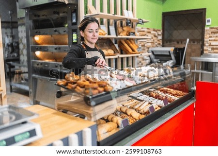 Baker skillfully arranging a tempting selection of pastries in a display case at a charming bakery shop, creating an inviting atmosphere