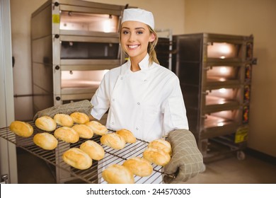 Baker smiling at camera holding rack of rolls in a commercial kitchen - Powered by Shutterstock