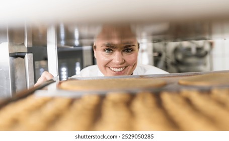 Baker smiling while checking trays of freshly baked cookies on a cooling rack in a bakery, inspecting the baked goods in a professional baking environment - Powered by Shutterstock