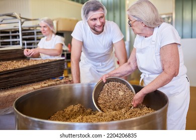 Baker Team With Apprentice Mixing Grains For Wholemeal Bread In Large Vat