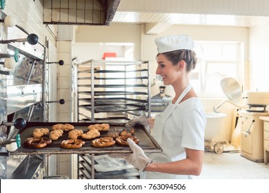 Baker woman getting bakery products out of oven on baking sheet - Powered by Shutterstock