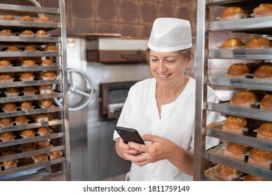 Baker woman smiling and texting with her phone surrounded by cupcakes - Powered by Shutterstock