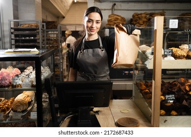 Baker Woman Standing With Fresh Bread And Pastry At Bakery. Young Woman In Her Bake Shop Looking At Camera. Satisfied Baker With Breads In Background. Girl Owner Bakery Shop
