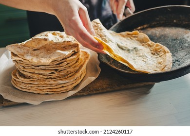 baker's hands are removing pita bread from a cast-iron frying pan. Private mini bakery producing craft bread and pita bread. baker in apron in kitchen puts ready-made pita bread in pile