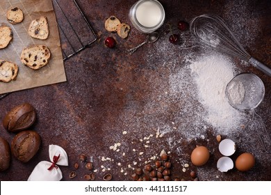 Bakery background, baking ingredients over rustic kitchen countertop. Baked cookies with hazelnuts, rye bread, milk and eggs. Top view, copy space.
