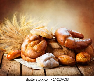 Bakery Bread on a Wooden Table. Various Bread and Sheaf of Wheat Ears Still-life. 