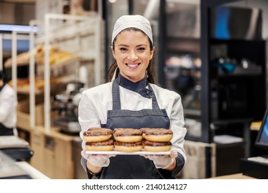 A bakery department worker in supermarket offering doughnuts and smiling at the camera. - Powered by Shutterstock