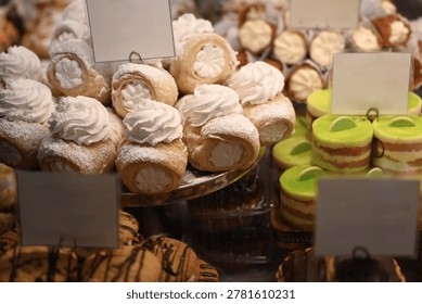 Bakery display case featuring puff pastry cream horns filled with whipped cream, alongside bright green layered cakes and chocolate cookies.