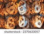A bakery display case filled with hanging pretzels with various toppings. Chocolate, cheese, nuts. Background.