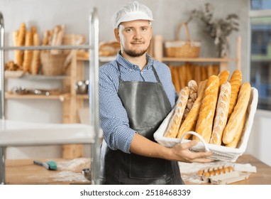 Bakery employee man holds basket of ready-made baguettes. Male baker holds basket with finished products, shows many different baguettes. - Powered by Shutterstock