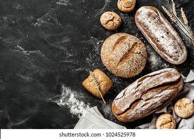 Bäckerei - goldene rustikale Krusteliebungen aus Brot und Brötchen auf schwarzem Kalkbrett-Hintergrund. Stillleben von oben erfasst (Draufsicht, flacher Lauf). Layout mit kostenlosem Text-Leerzeichen.