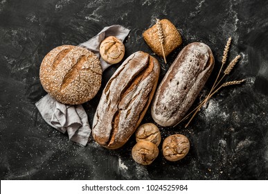 Bäckerei - goldene rustikale Krusteliebungen aus Brot und Brötchen auf schwarzem Kalkbrett-Hintergrund. Stillleben von oben erfasst (Draufsicht, flacher Lauf).